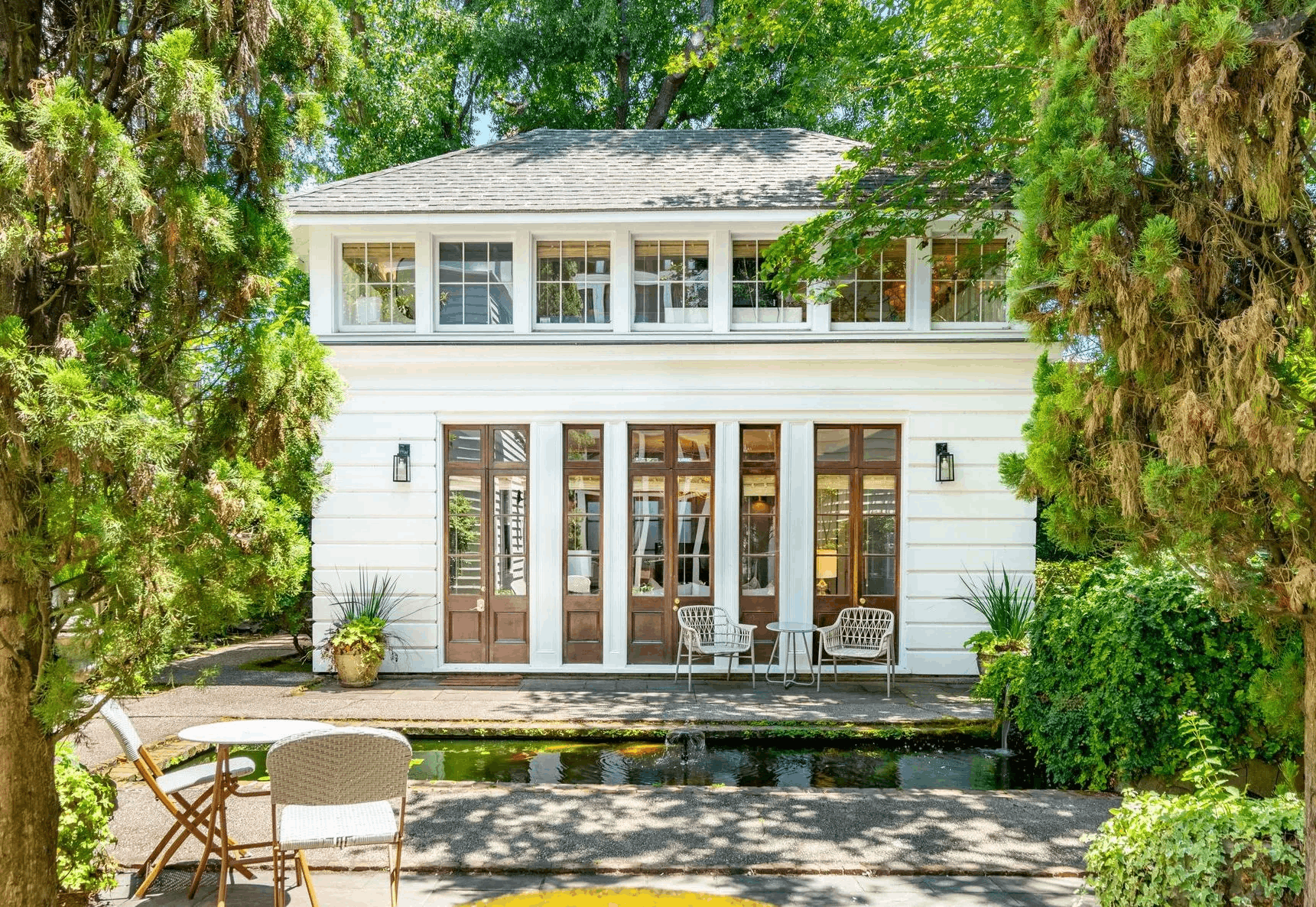 A beautiful two-story CHC Vacation Rentals home with white siding, French doors, a backyard pond, and a lush green garden