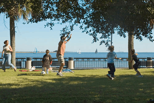 A family enjoying a sunny day playing soccer on the grassy lawn at Waterfront Park in Charleston, SC.