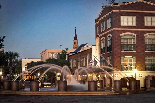 Evening view of the illuminated splash fountain at the entrance of Waterfront Park in downtown Charleston, with historic buildings