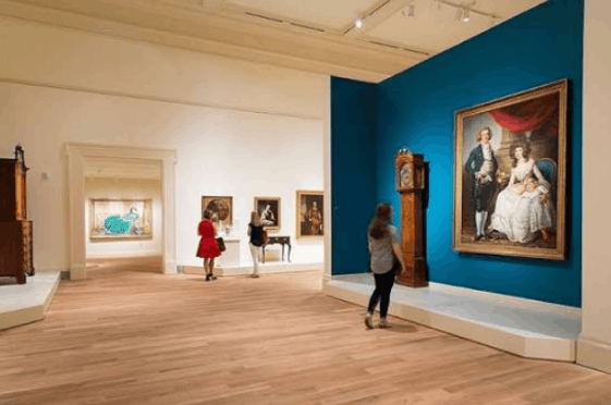 Visitors viewing classic portrait paintings and historical furniture inside a
  gallery at the Gibbes Museum of Art in Charleston, South Carolina.